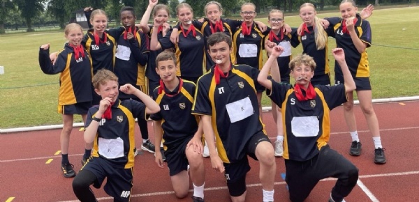 Kennet Year 7 pupils celebrating their District Sports Day success by holding their medals in their teeth and smiling for the camera.