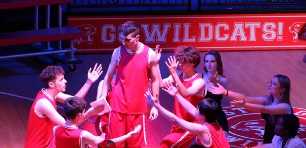 Pupils from Kennet School perform a dynamic basketball team scene during their high school musical production, dressed in team uniforms mid-action on 
