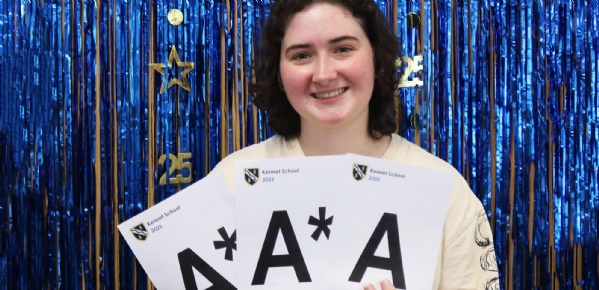 Kennet Student Clara celebrates her A Level results holding up cards of her grades against a blue foil curtain